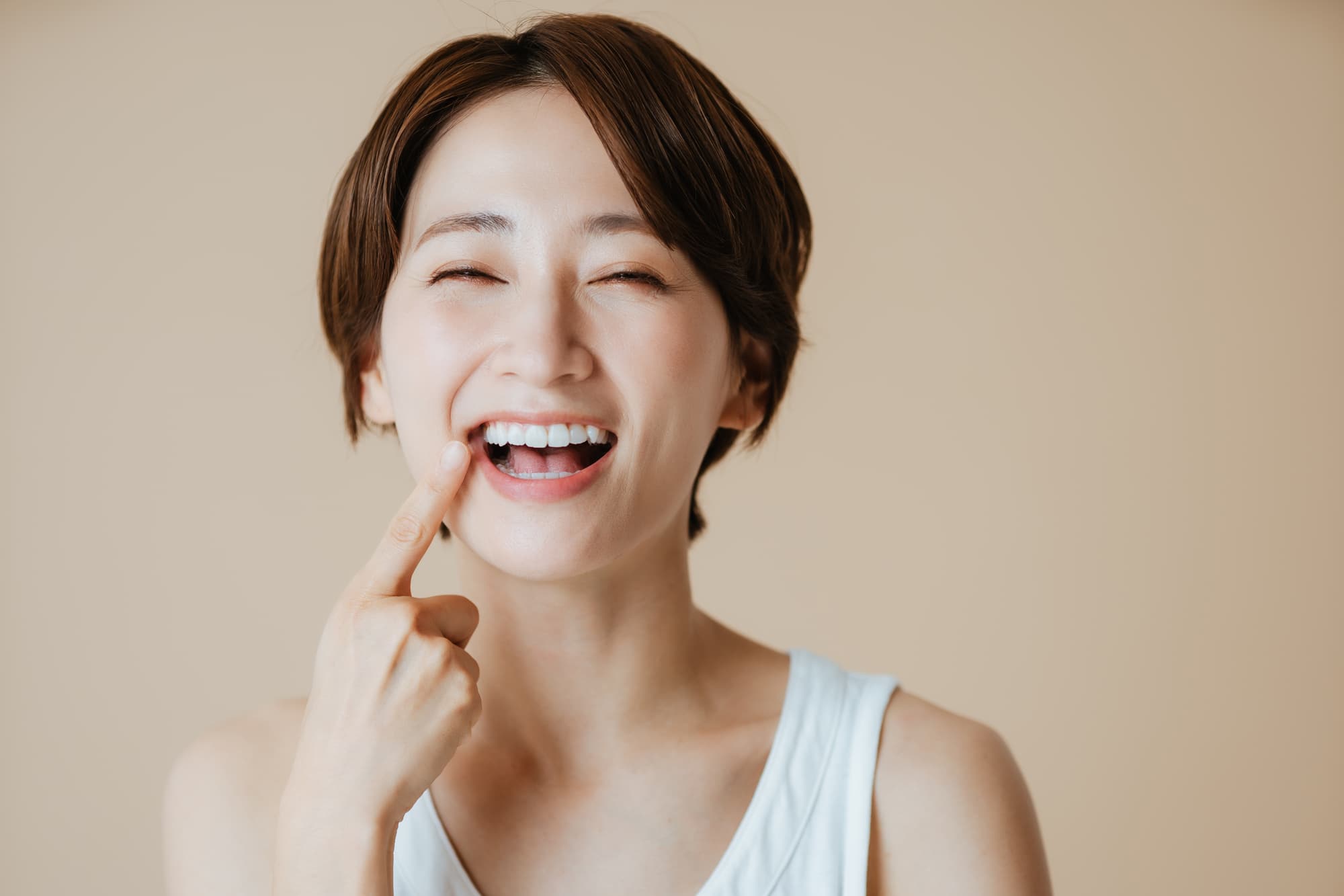 セラミック治療できれいになった歯を指さし笑顔の女性