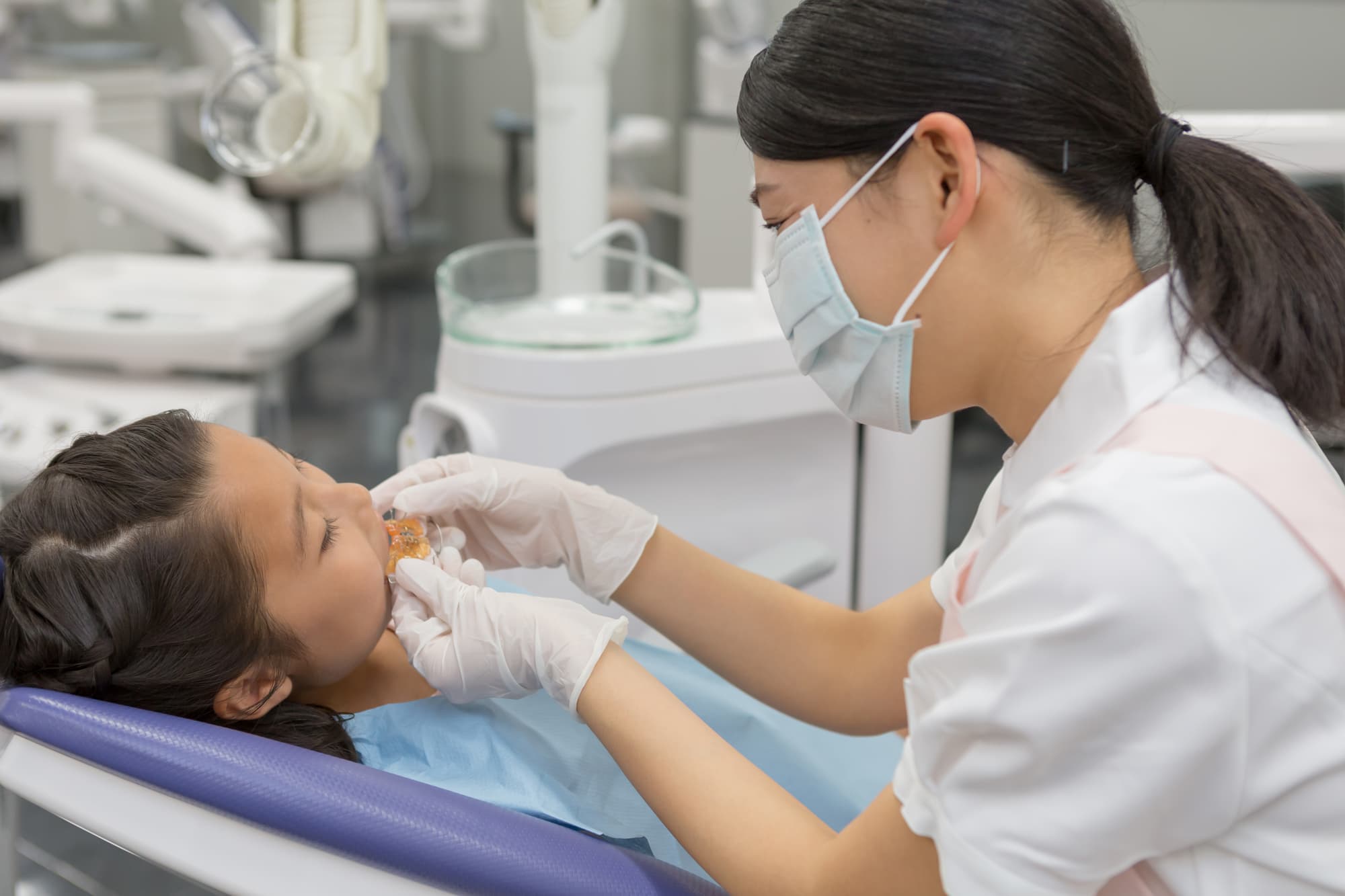 女の子に床矯正の装置を装着する歯科衛生士の女性