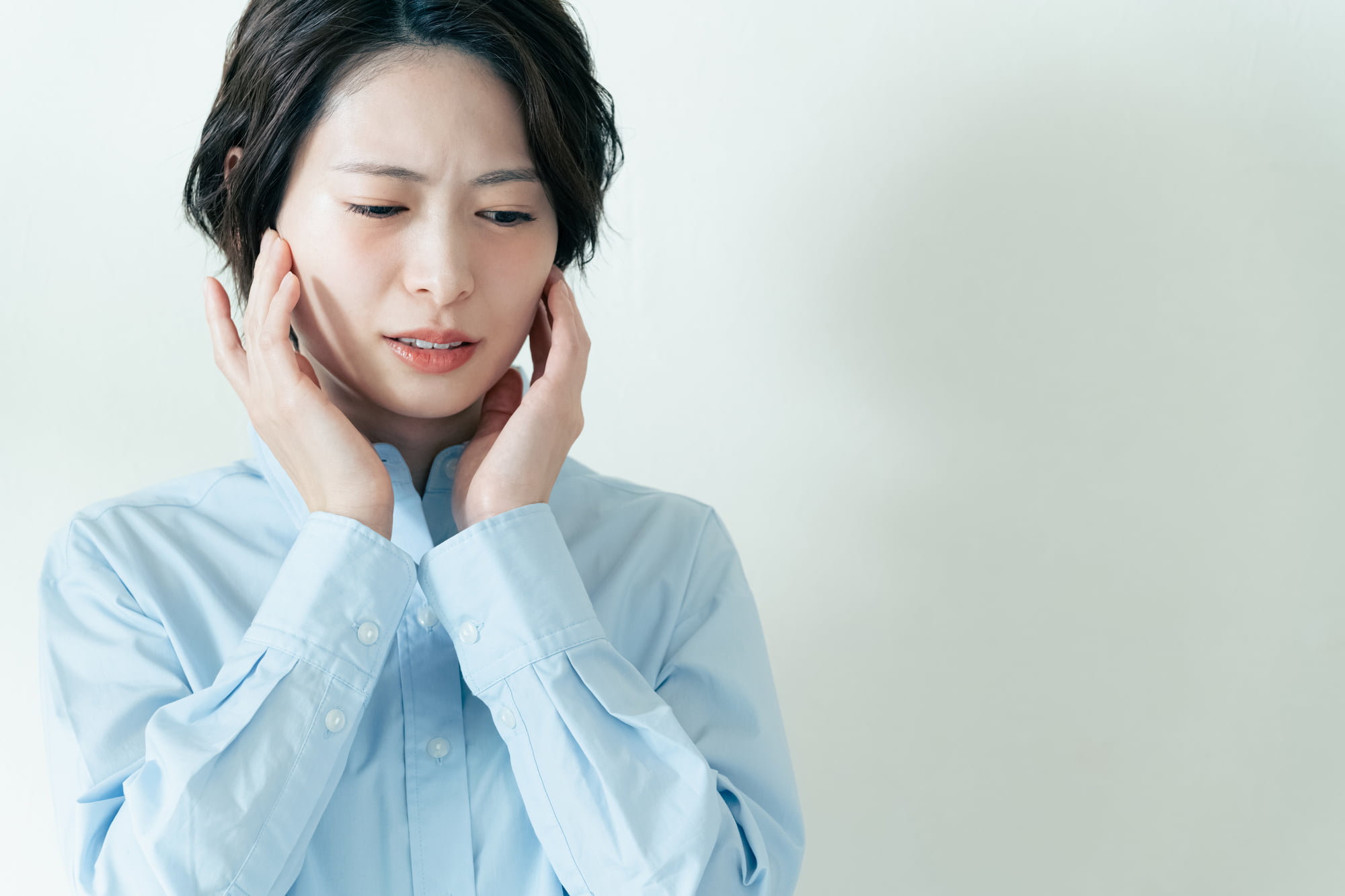 顎関節症で痛む顎を両手でおさえる女性